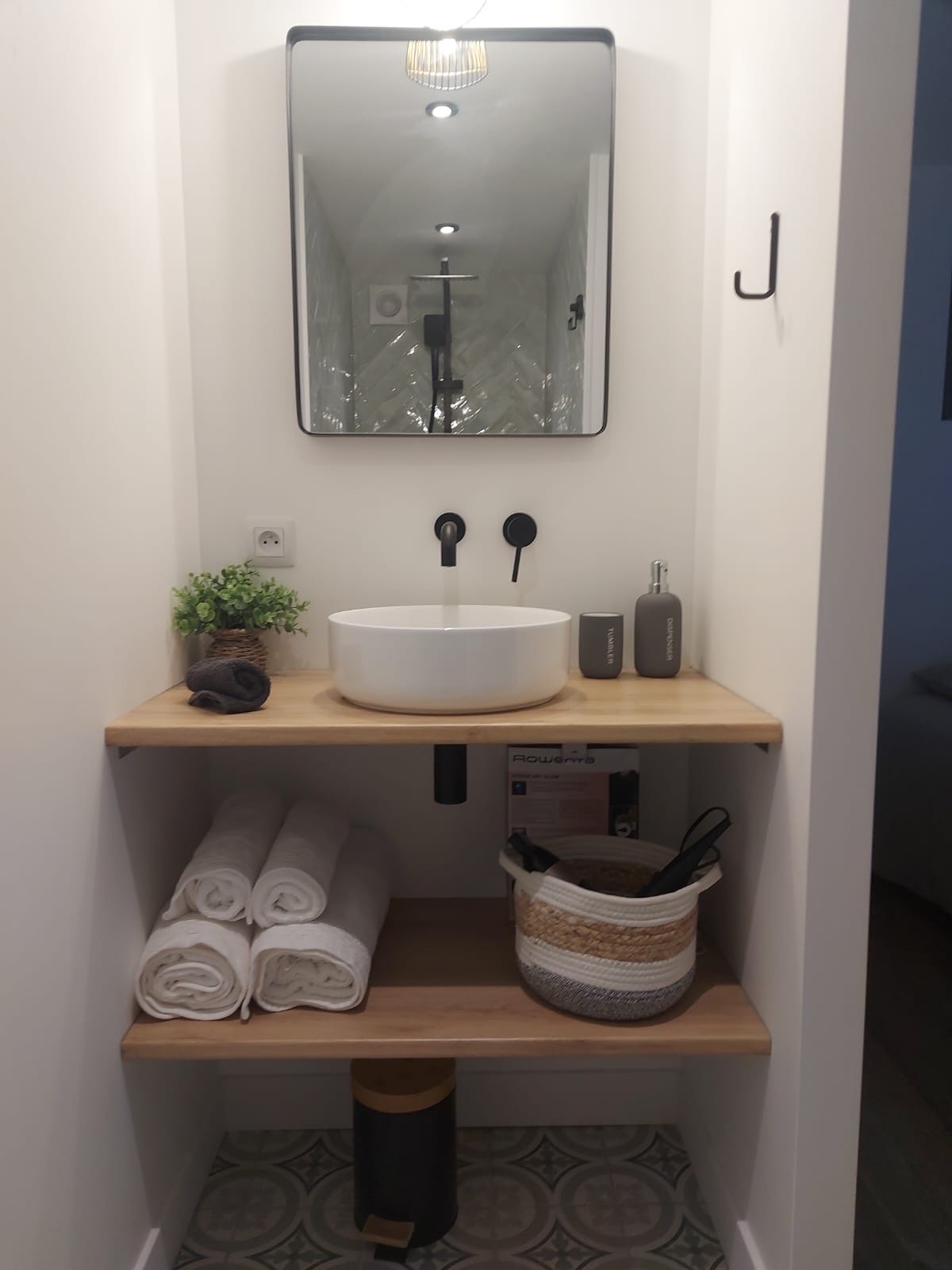 Bathroom vanity with vessel basin, matte-black taps, rolled towels and patterned cement floor tile
