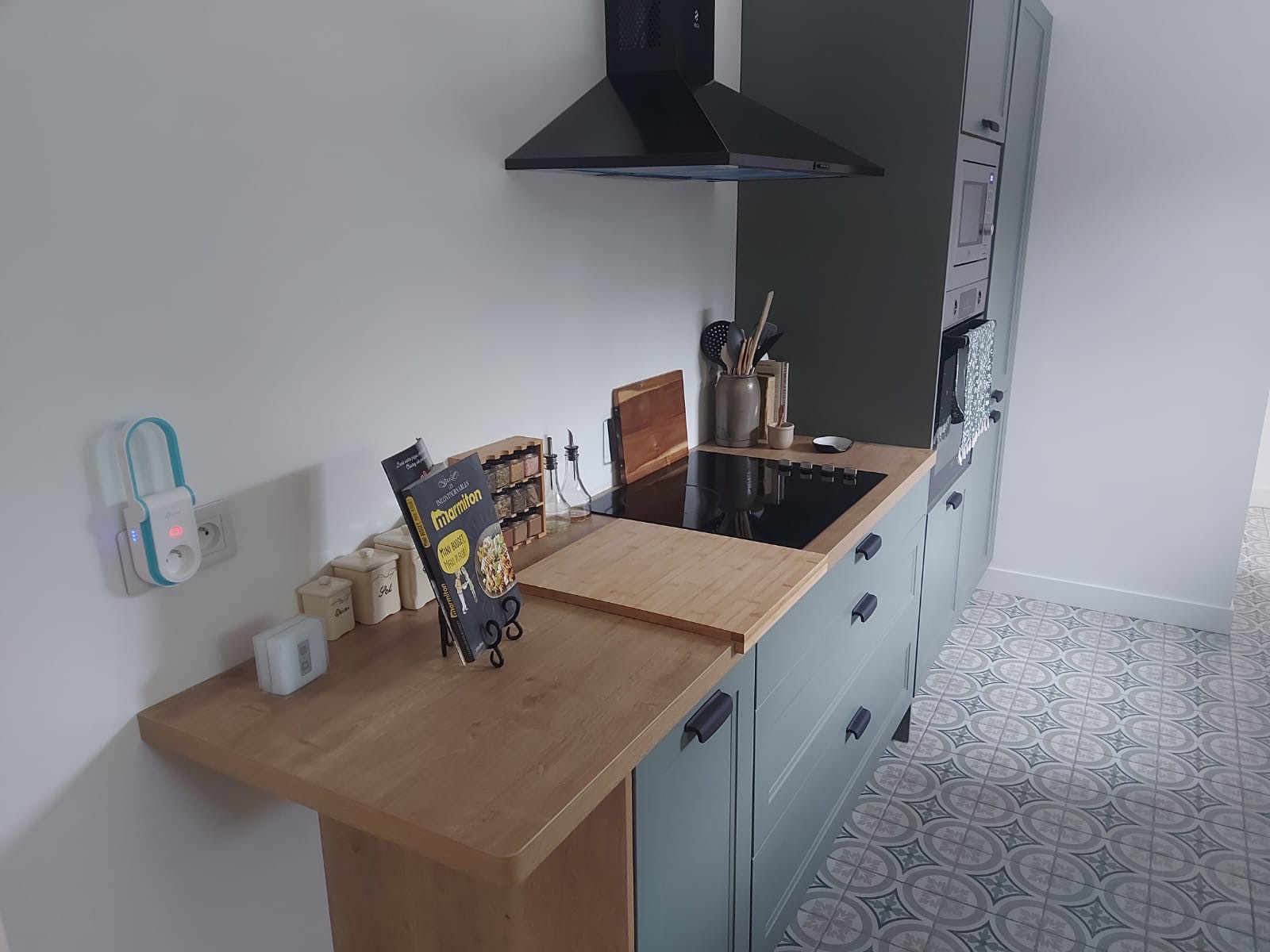 Kitchen hob and extractor with sage cabinets and patterned cement floor tile
