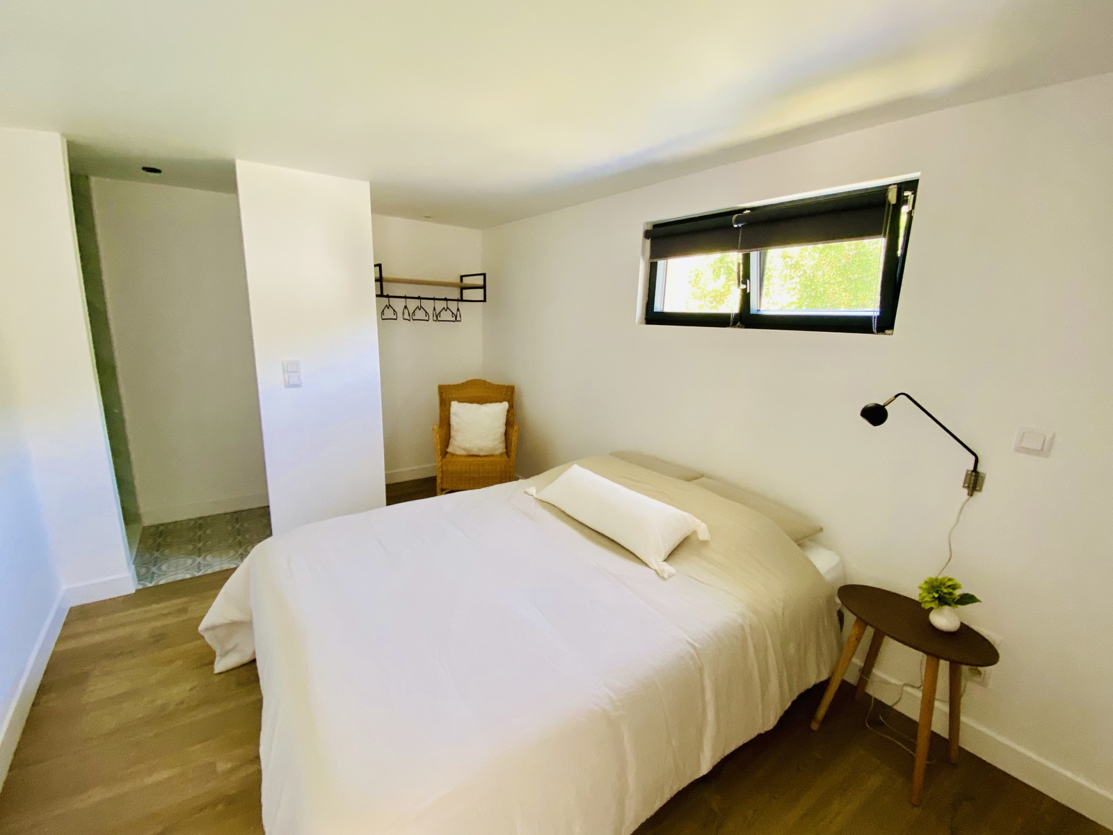 Ground-floor bedroom with crisp white linen, rattan chair and view through to the en-suite cement tile
