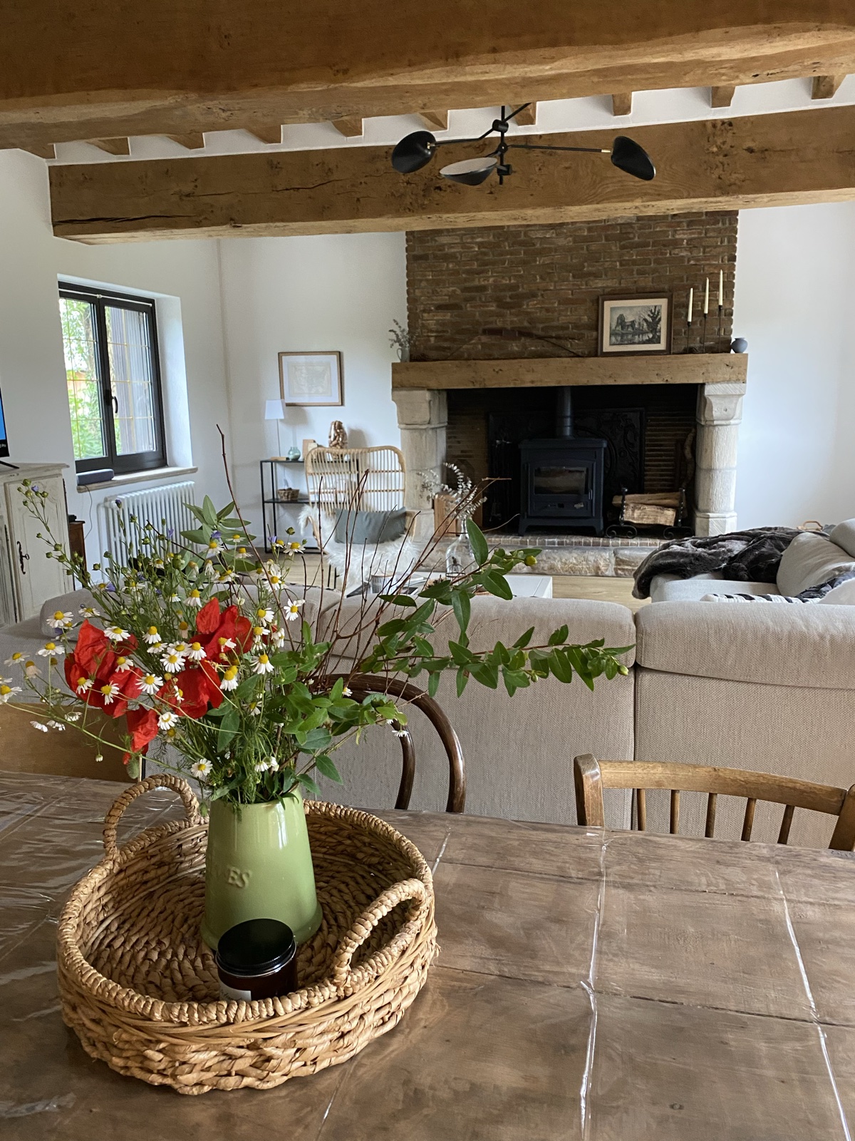 A wildflower bouquet of poppies and daisies on the dining table, salon and stone fireplace beyond