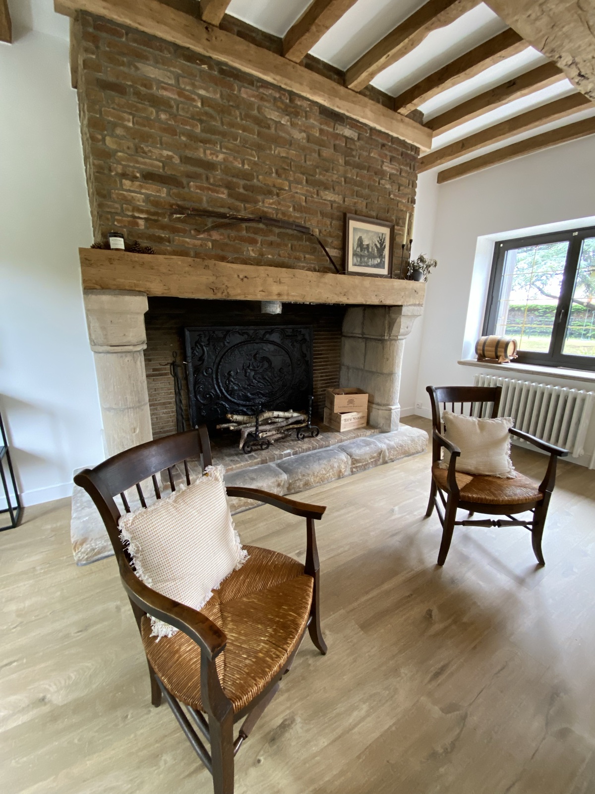 Two rush-seat antique chairs flanking the brick-and-stone fireplace under exposed beams